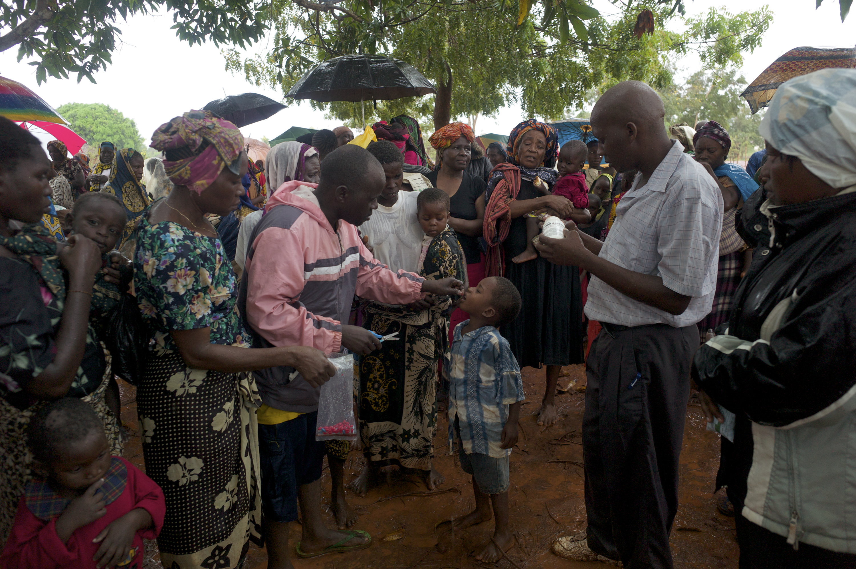 May 6, 2014 - Ganze sub-county (within Kilifi county), Kenya - Standing in the rain at an outreach site, children receive doses of vitamin A from  Madamani Dispensary community health workers Francis Kadenge (administering the dose) and Amos Mkare (holding the bottle of vitamin A) during Malezi Bora. (Photo by Ric Francis)